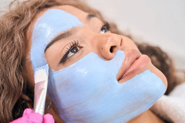 Beautician Applies Blue Mask Brush Forehead Cheeks Beautiful Woman Procedure — Foto de Stock