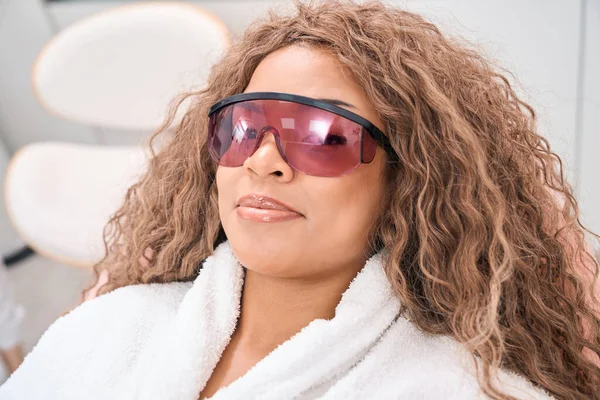Woman in a medical beauty center lies on a couch in protective glasses