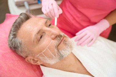 Kadın elleri, erkek yüzüne smas kaldırmadan önce işaretler çizer. Donanım kozmetolojisi. Cerrahi olmayan yüz kaldırma. Yenilenme süreci. Spa tedavisi.