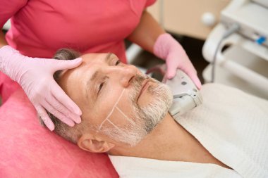 Kadın elleri, erkeğin boynunu kaldıran aultrasonik yüz gerdirme ameliyatı yapıyor. Cerrahi olmayan yüz kaldırma. Yenilenme süreci. Donanım kozmetolojisi