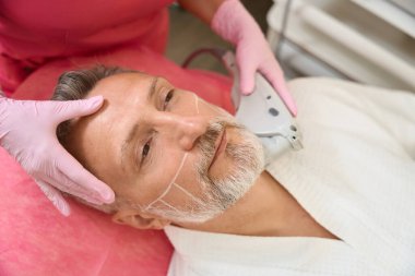 Cildiyeci doktorun elleri, erkeklerin ultrasonda yüz gerdirme ameliyatını kaldırıyor. Hasta yüzüne yakın çekim.