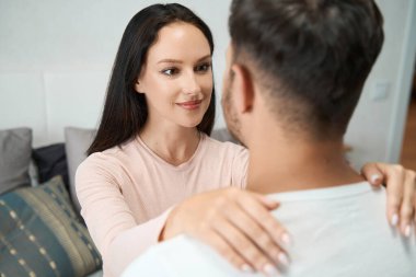 Woman put her hands on the strong shoulders of the man and looks into his eyes with love and trust