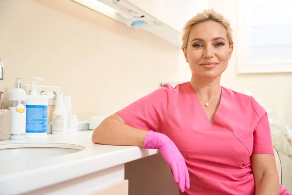 Waist Smiling Female Beautician Sitting Chair Leaning One Hand Table — стоковое фото