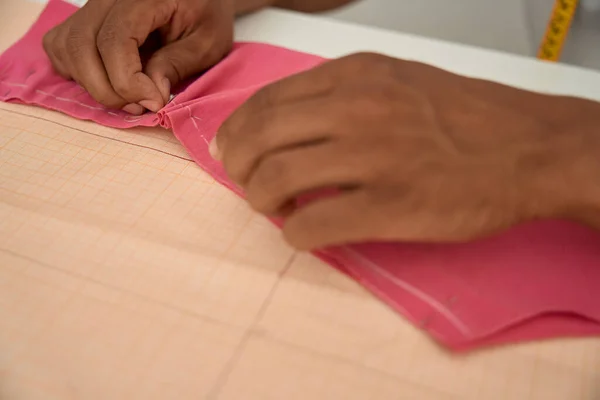 Top view cropped head close up of man hands using needle on fabric during working process at desk