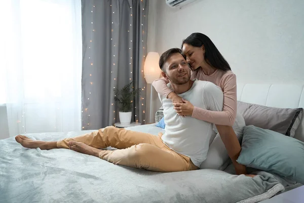 Cute young man and woman are chatting comfortably at home on bed they are comfortable in each other arms