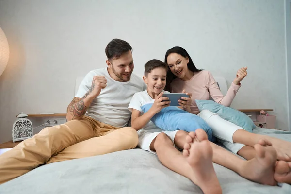 Friendly dad, mom and son spend time together looking at wonderful family photos on the phone