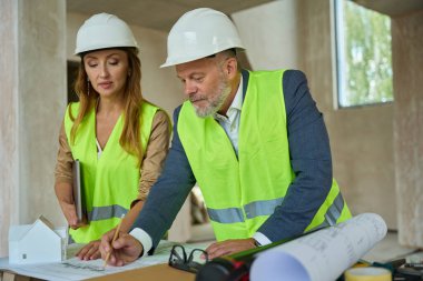 manager watches as the foreman draws with a pencil on the drawing on the table. Inspection of an unfinished house