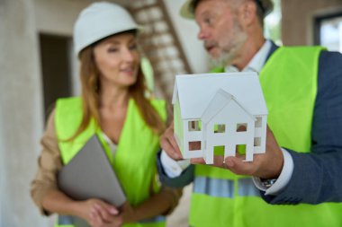 Foreman shows real estate agent a small model of a house under construction