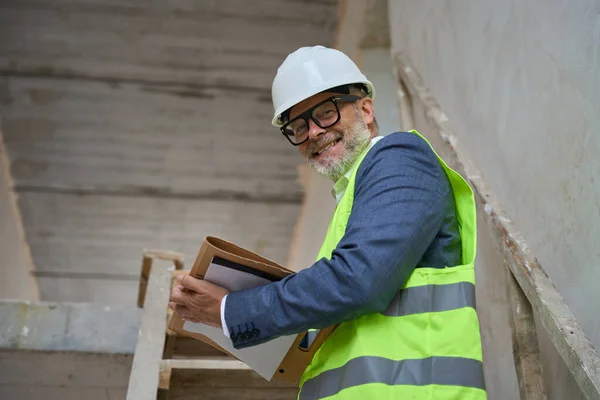 Happy Foreman Helmet Holding Folder While Standing Stairs Unfinished Cottage — Foto de Stock