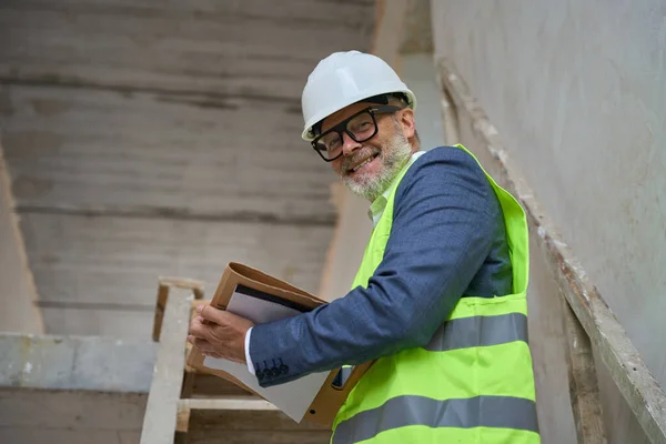 Happy Foreman Helmet Holding Folder While Standing Stairs Unfinished Cottage — Foto Stock