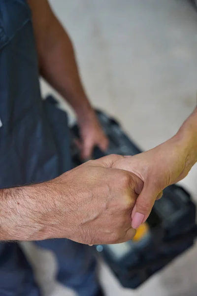 Female hand shakes builder male hand against the background of tool box. Close up photo