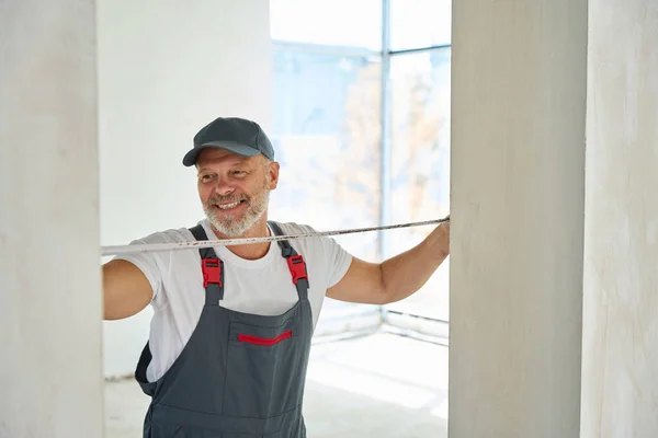 Joyful Gray Haired Builder Measures Width Doorway Tape Measure Photo — ストック写真