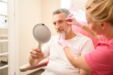 Man looking in the mirror when the beautician examines his face. Cropped photo