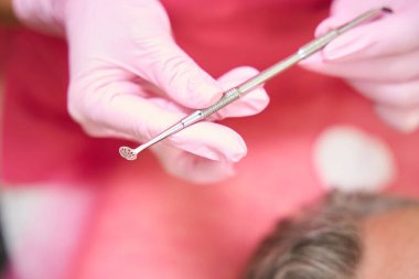 Female hands in pink gloves hold uno spoon in beauty salon. Cropped photo