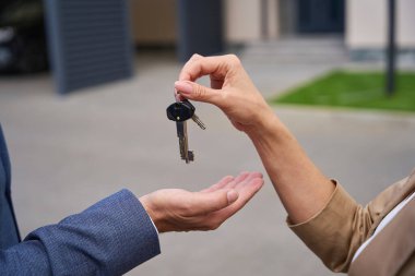 Female hand puts in male palm keys to house countryside. Close up photo. Against background of grass and the road