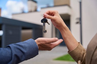 Close-up of woman hand passing keys to man hand. Against the backdrop of a beautiful modern house