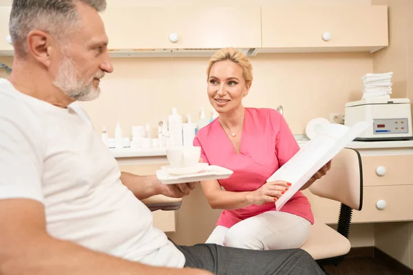 Beautiful cosmetologist woman shows the price list to the client and advises him over coffee