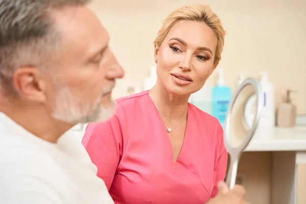 Man looks in mirror at consultation with beautician. Cropped photo