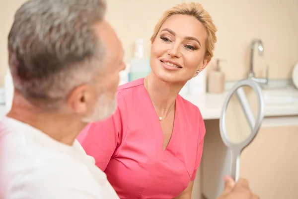 Bearded man looks in the mirror at a consultation with a woman beautician. Cropped photo