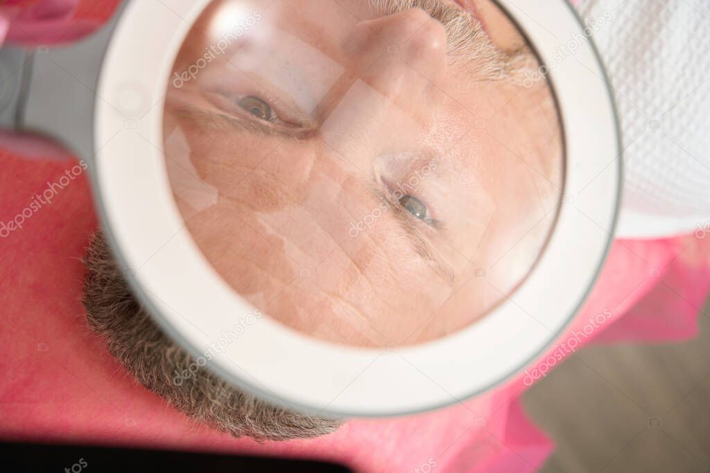 Face of man under magnifying glass in spa salon. Cropped photo