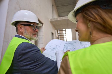 Smiling female realtor discussing a project with a male foreman while standing inside an unfinished house