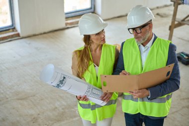Foreman man holds an open folder and discusses with the real estate manager. They stand in an unfinished building