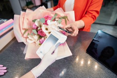 Close-up paying for order by phone through terminal in flower shop. There is fashionable bouquet on counter
