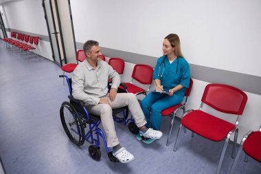 Optimistic patient in a wheelchair communicates with a friendly attending physician in the lobby of an outpatient clinic