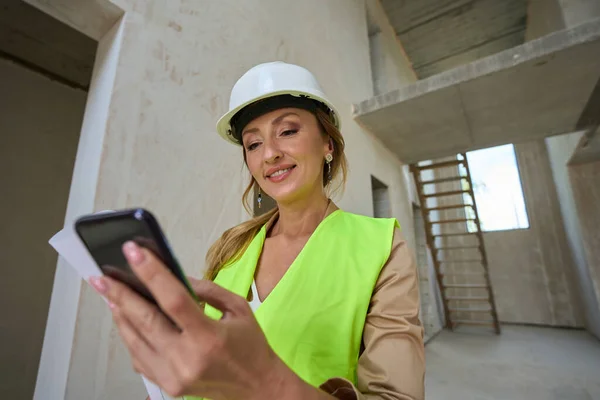 Pretty Real Estate Sales Manager Looking Mobile Phone Holding Blueprints —  Fotos de Stock