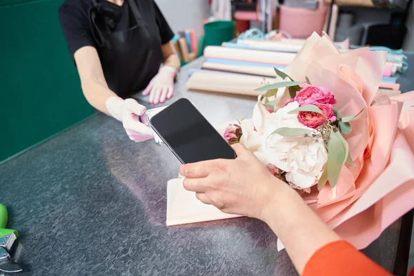 Online payment for ordering bouquet of flowers by phone through terminal. Woman picking up her order at flower boutique