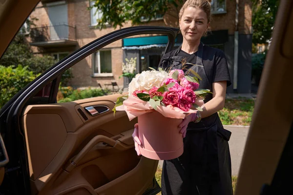 Charming female florist opened side door of car to give luxurious bouquet of flowers. Online order in flower shop