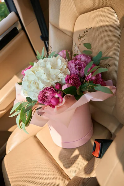 Charming author bouquet in pink box stands on leather seat inside car. Online ordering bouquets from florist in flower boutique