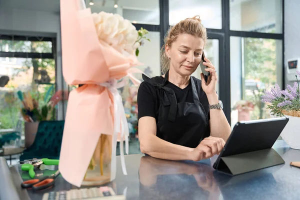 Attentive florist takes online order by phone, entering data into working tablet. Creation of original bouquets of flowers