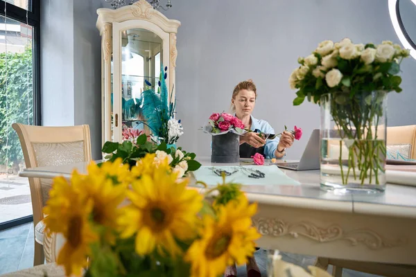 Florist shows how to create bouquet of flowers in box on online master class. Woman in store with luxury interior