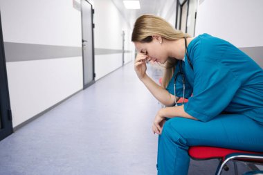 Doctor with long hair sits in a bright corridor on a red chair