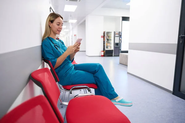 Adult Woman Doctor Sits Corridor Chair Looks Phone — Stock fotografie