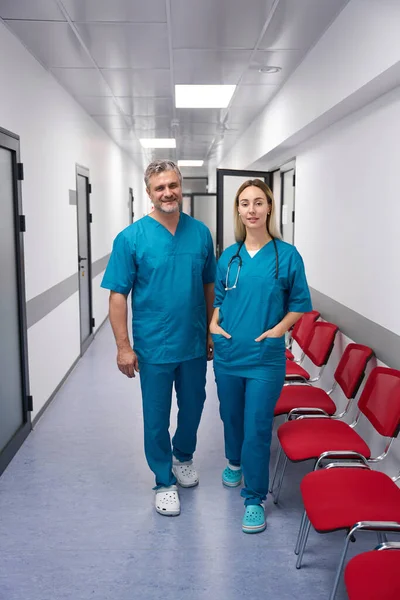 Woman doctor and a man doctor are standing in a bright corridor smiling