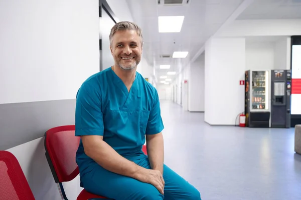 Doctor Blue Doctor Uniform Smiling While Sitting Hospital Lobby — Zdjęcie stockowe