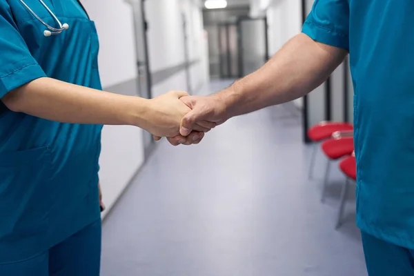 Male doctor and female doctor shaking hands in hospital lobby