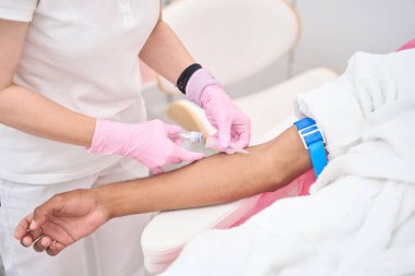 Cropped photo of experienced clinical nurse inserting syringe needle into patient vein