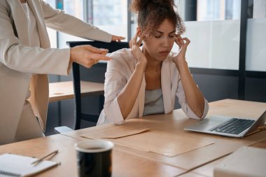 Woman is talking to a tired work colleague who covers her ears to focus. Coworking business