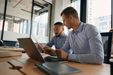 Two men are discussing documents in their hands, being in an office with panoramic windows