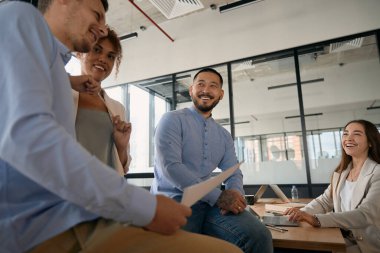 Team of young employees chatting and laughing while being in an open office with large windows