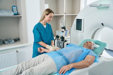 Blonde nurse in blue clothes injects medicine into a patients hand in a medical center