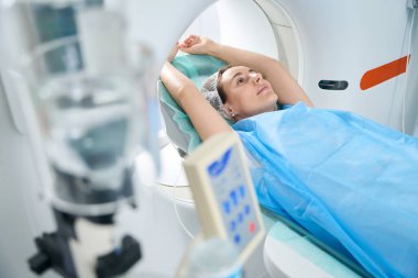 Young pretty woman with her arms outstretched up in disposable clothing is placed in a tomograph camera for computed tomography