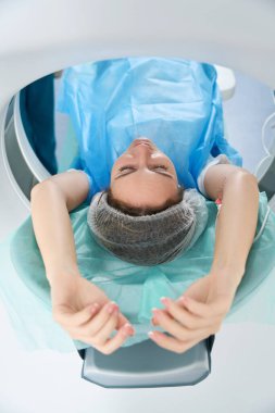 Young woman in disposable clothes is placed in a tomography camera in a modern medical center