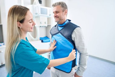 Gray-haired man stands while he is put on a protective coat