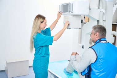 Doctor adjusts x-ray machine while man in protective coat waits