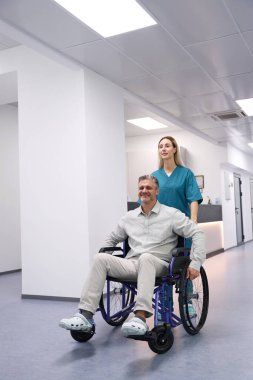 Doctor in a blue uniform carries a patient in a wheelchair along the corridor of the hospital