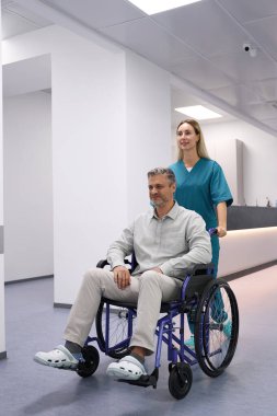 Doctor in a blue uniform drives a patient in a wheelchair along the corridor of the hospital
